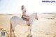 A woman in a bikini riding a white horse in the desert.