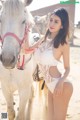 A woman in a white lingerie standing next to a white horse.