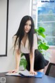 A woman in a white shirt and black skirt leaning over a desk.