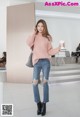 A woman in a pink sweater and jeans holding a cup of coffee.