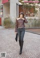 A woman walking down a brick walkway wearing a brown jacket and black boots.