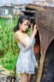 A woman in a white dress leaning against an old rusty truck.