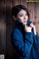 A woman in a denim jacket leaning against a wooden wall.