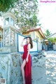 A woman in a red dress leaning against a stone wall.