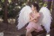 A woman in a pink dress sitting on a tree branch with white wings.