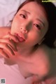 A naked asian woman laying on a bed with her hand on her chin.