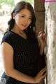 A woman leaning against a stone wall in a black dress.