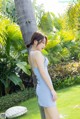 A woman in a blue dress leaning against a palm tree.