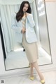 a woman standing in front of a mirror wearing a blue blazer and beige skirt