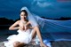 A woman in a wedding dress sitting on a dock.